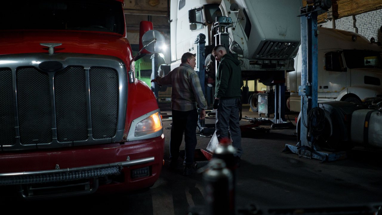 Two mechanics inspecting heavy-duty trucks in an indoor service garage