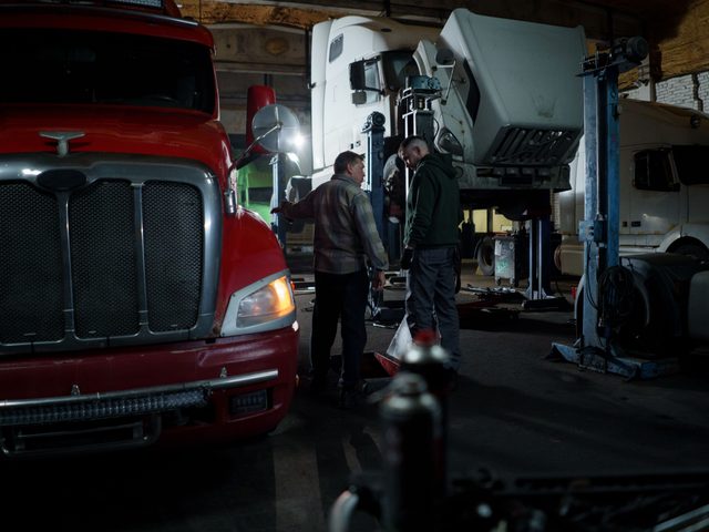 Two mechanics inspecting heavy-duty trucks in an indoor service garage